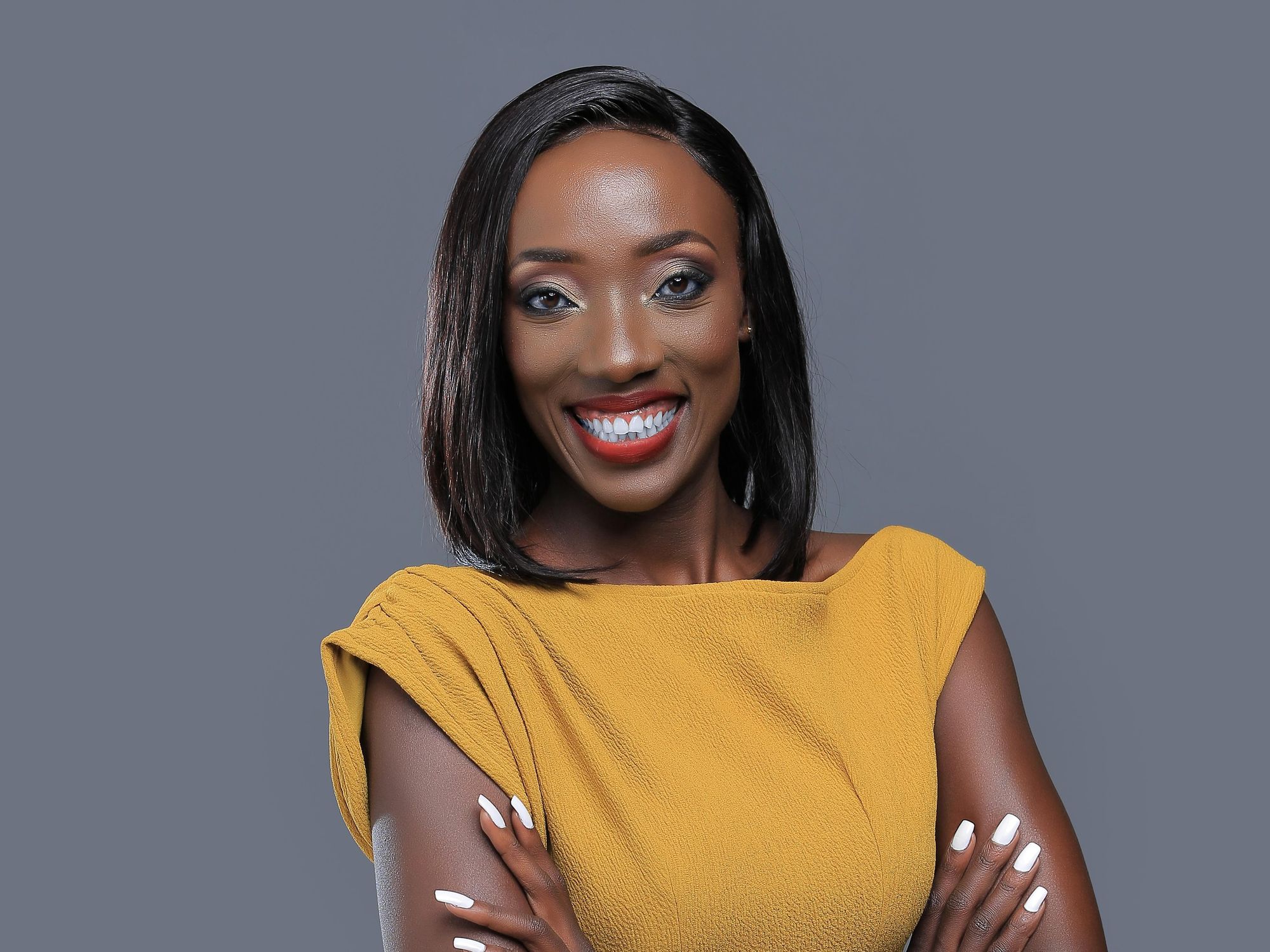 Usher Komugisha, a Ugandan sports analyst and journalist, wearing a mustard dress and folding her arms. 
