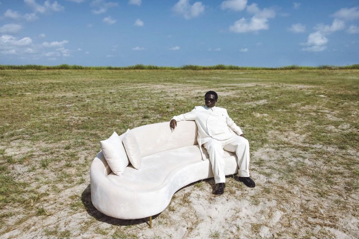 Wande Coal sits on a white couch in an open field.