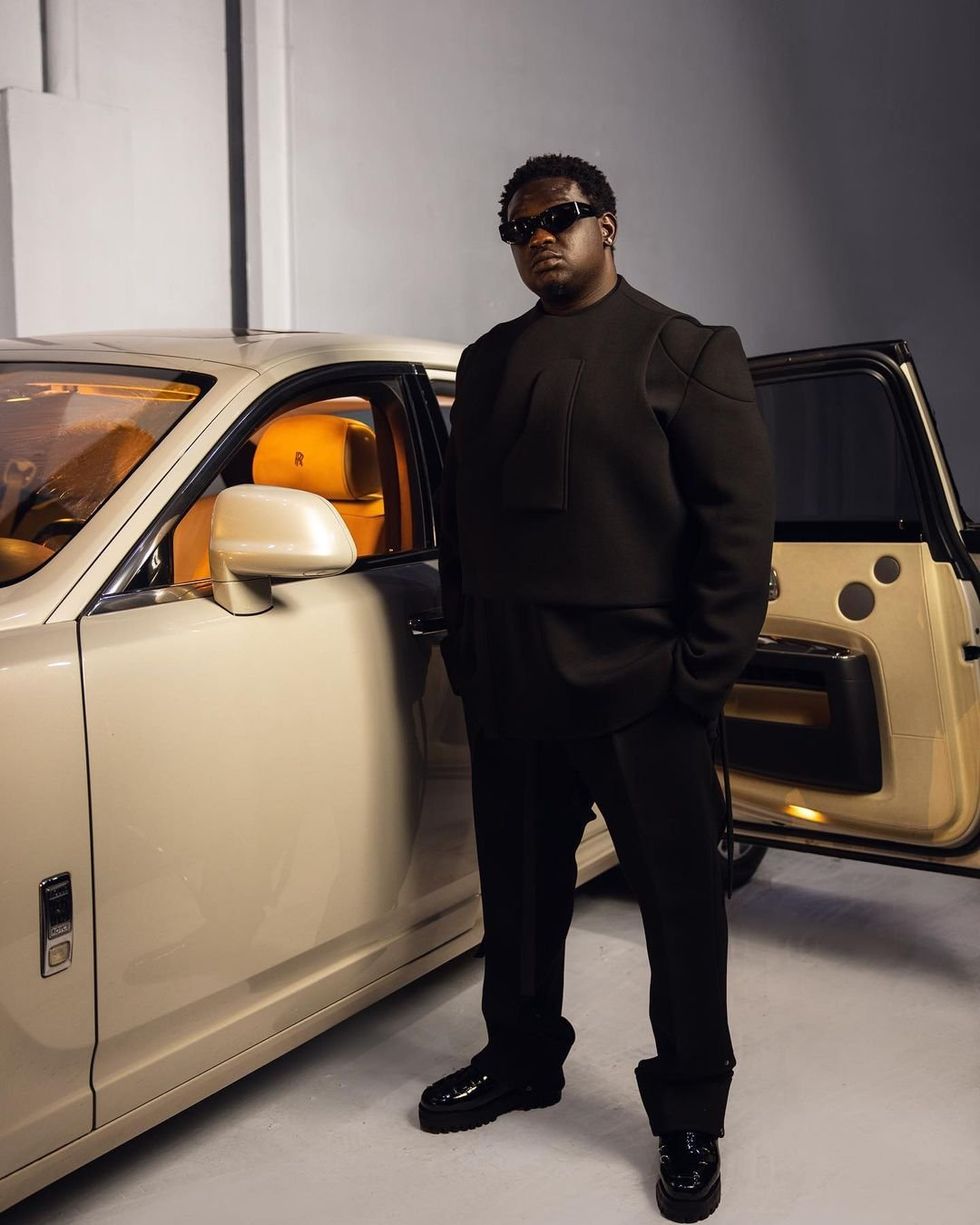 Wande Coal stands in front of a fancy car.