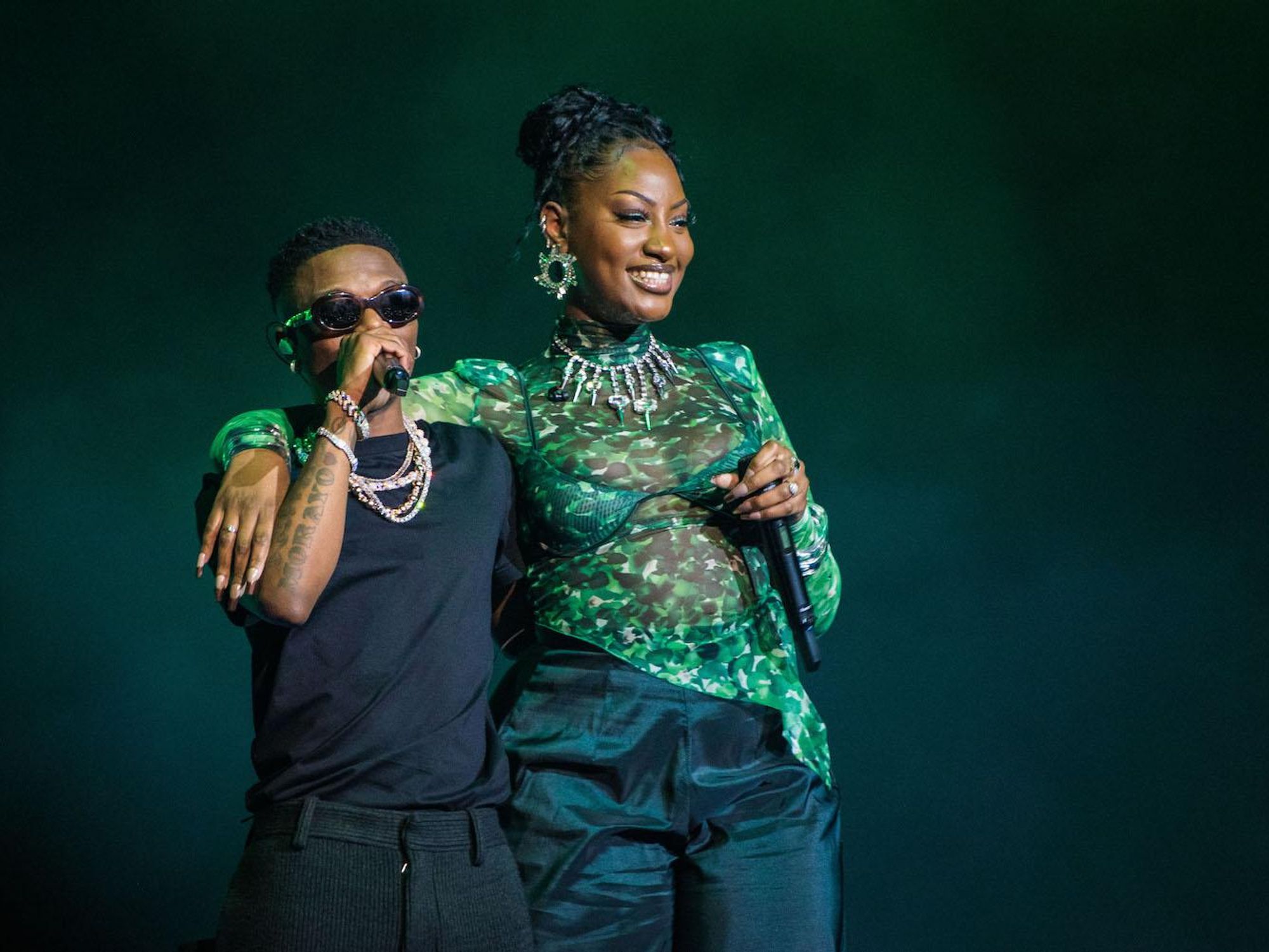 Wizkid and Tems performing together wearing green shirt and sunglasses.  