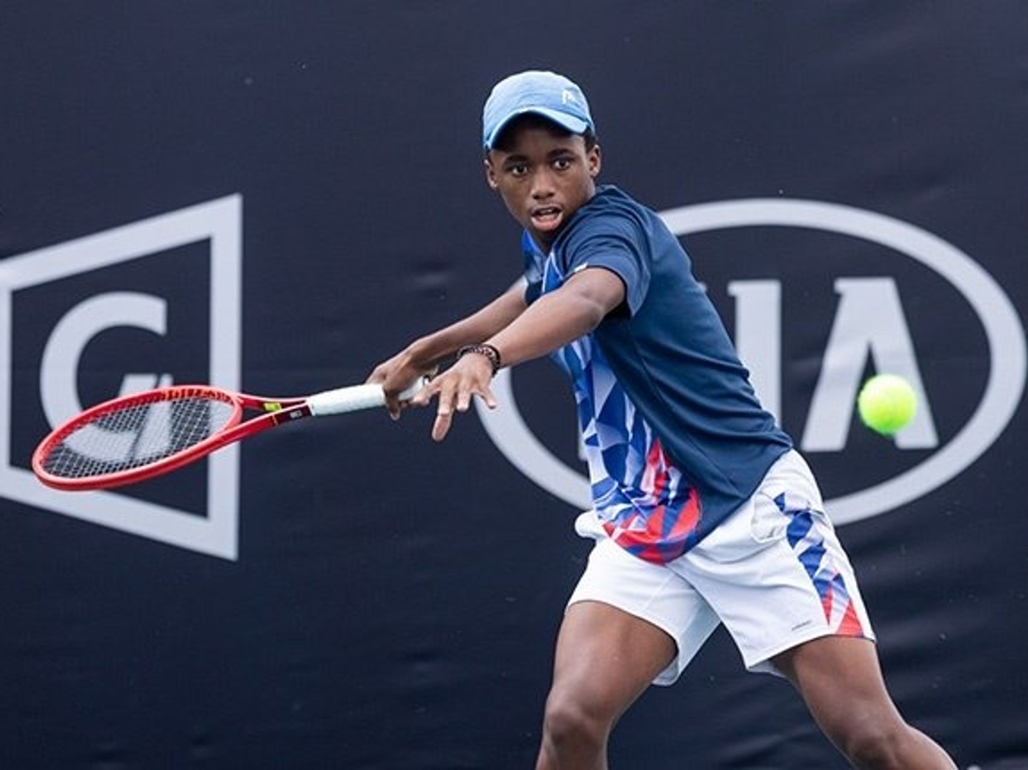 Young black man playing tennis wearing white shorts and blue top.