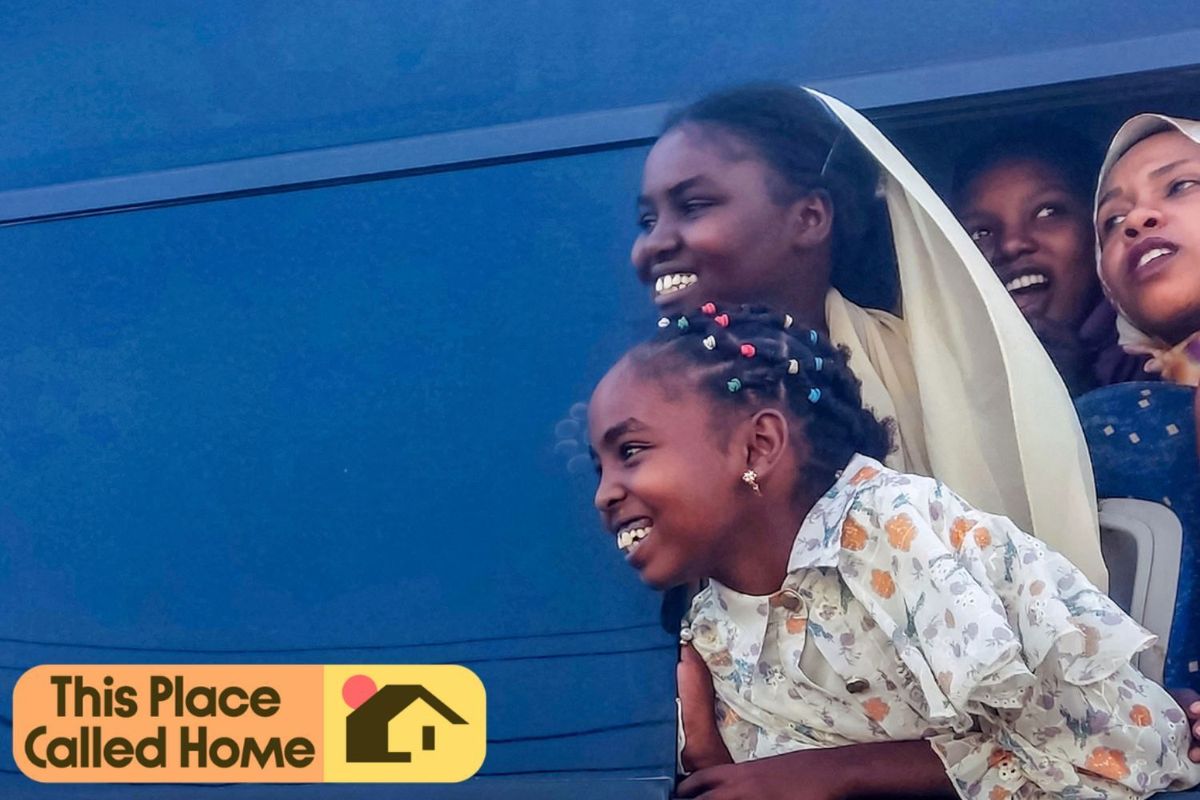 Young girls smiling with their heads out the window of a bus.